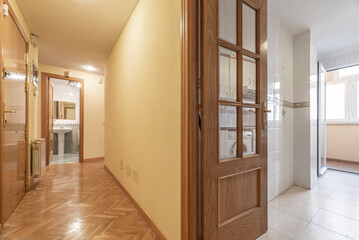 Distributor corridor of a house with oak carpentry with wooden and glass doors, kitchen tiles with border, matching herringbone parquet and aluminum radiators