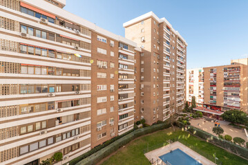 Facade of an urban residential apartment building with swimming pools and common areas, gardens and playgrounds on a sunny day without clouds