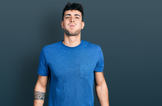 Young hispanic man wearing casual t shirt puffing cheeks with funny face. mouth inflated with air, crazy expression.