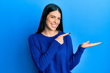 Young hispanic woman wearing casual clothes amazed and smiling to the camera while presenting with hand and pointing with finger.