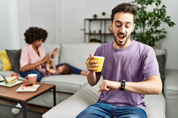 Hispanic father of interracial family drinking a cup coffee looking at the watch time worried, afraid of getting late