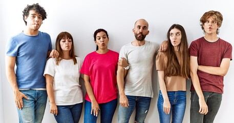 Group of young friends standing together over isolated background making fish face with lips, crazy and comical gesture. funny expression.