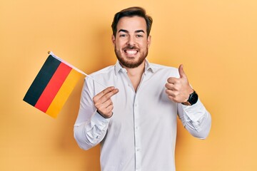 Handsome caucasian man with beard holding germany flag smiling happy and positive, thumb up doing excellent and approval sign