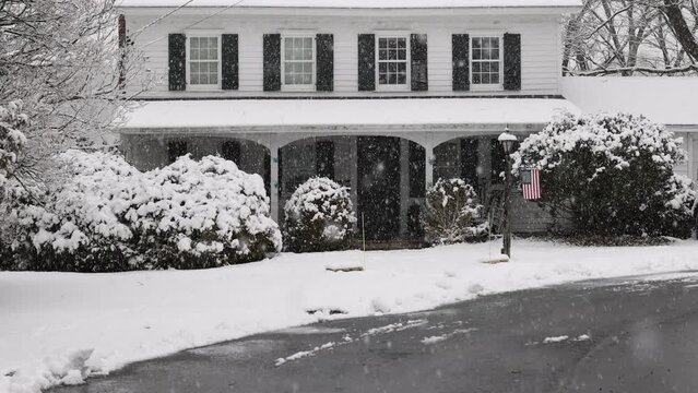 Snow falling in slow motion in front of historic home with American flag
