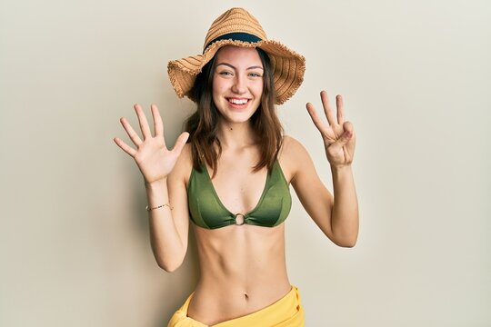 Young brunette woman wearing bikini showing and pointing up with fingers number eight while smiling confident and happy.