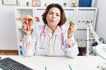 Middle age hispanic doctor woman holding anatomical female genital organ and birth control pills...