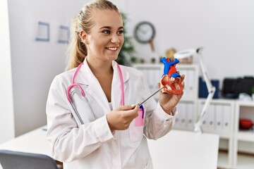 Young blonde girl wearing doctor uniform holding heart at clinic