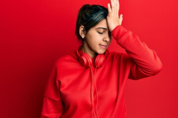 Young latin woman listening to music using headphones surprised with hand on head for mistake, remember error. forgot, bad memory concept.