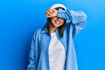 Young latin woman wearing cute wool cap covering eyes with arm smiling cheerful and funny. blind concept.
