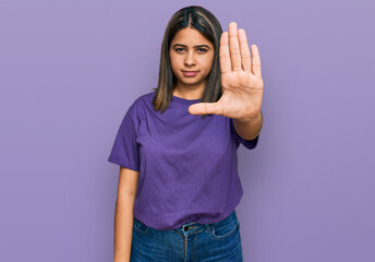 Young hispanic girl wearing casual purple t shirt doing stop sing with palm of the hand. warning expression with negative and serious gesture on the face.