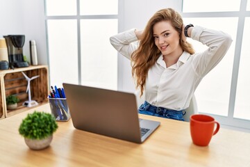 Young caucasian woman working at the office using computer laptop relaxing and stretching, arms and hands behind head and neck smiling happy