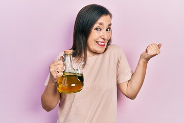Middle age hispanic woman holding olive oil can screaming proud, celebrating victory and success...