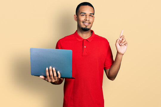 Young african american man working using computer laptop surprised with an idea or question pointing finger with happy face, number one
