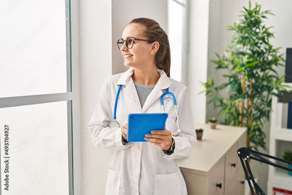 Poster young blonde woman wearing doctor uniform using touchpad working at clinic