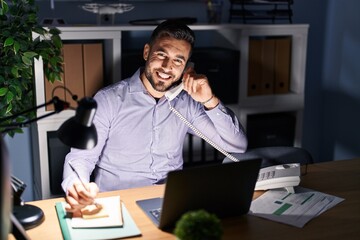Obraz premium Young hispanic man business worker talking on the telephone working overtime at office