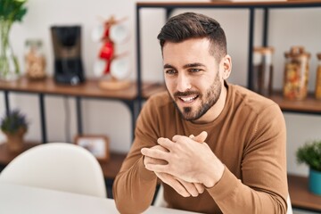 Young hispanic man smiling confident sitting on table at home