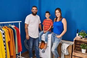 Family of three at laundry room looking positive and happy standing and smiling with a confident smile showing teeth