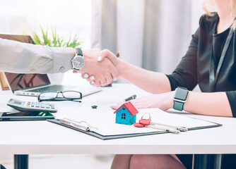businessman in a shirt and a blue tie in the office and a business woman in a dress shake hands after signing contracts about a sold house.