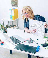 businesswoman in a blue suit sits at a desk in the office and shows hand-drawn graphs to partners using a video chat. Strategy business concept