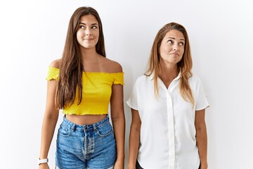 Mother and daughter together standing together over isolated background smiling looking to the side and staring away thinking.