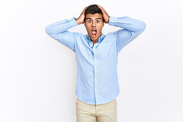 Young hispanic man wearing business shirt standing over isolated background crazy and scared with hands on head, afraid and surprised of shock with open mouth