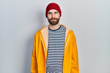 Caucasian man with beard wearing yellow raincoat smiling looking to the side and staring away thinking.