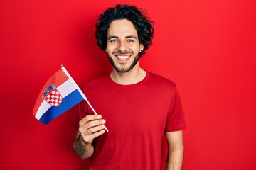 Handsome hispanic man holding croatia flag looking positive and happy standing and smiling with a confident smile showing teeth