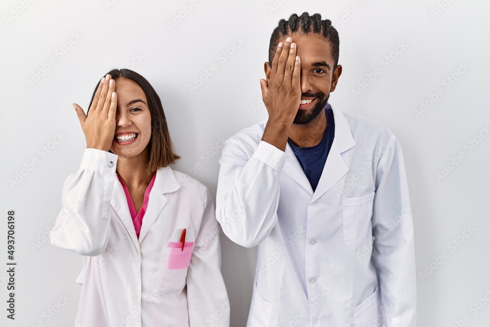 Sticker young hispanic doctors standing over white background covering one eye with hand, confident smile on