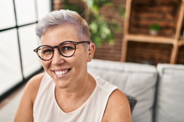 Middle age woman using hearing aid sitting on sofa at home