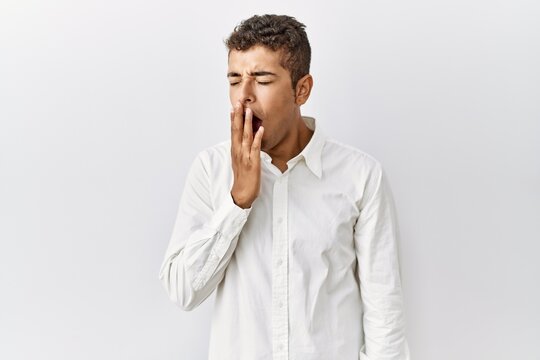 Young handsome hispanic man standing over isolated background bored yawning tired covering mouth with hand. restless and sleepiness.