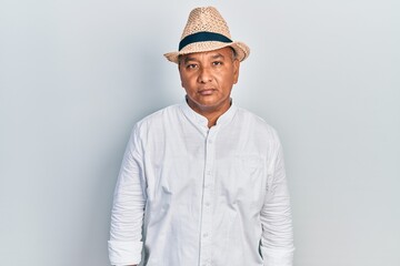 Middle age latin man wearing casual clothes and hat with serious expression on face. simple and natural looking at the camera.