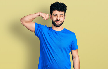 Young arab man with beard wearing casual blue t shirt strong person showing arm muscle, confident and proud of power