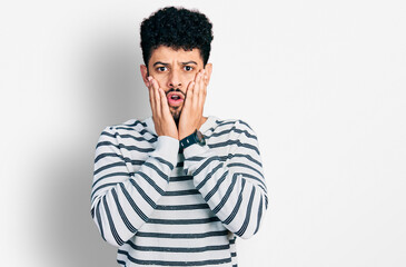 Obraz na płótnie Canvas Young arab man with beard wearing casual striped sweater afraid and shocked, surprise and amazed expression with hands on face