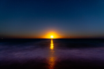 night sky with moonrise over ocean with long exposure of waves crashing on beach. empty space in sky