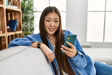 Young chinese girl using smartphone sitting on the sofa at home.