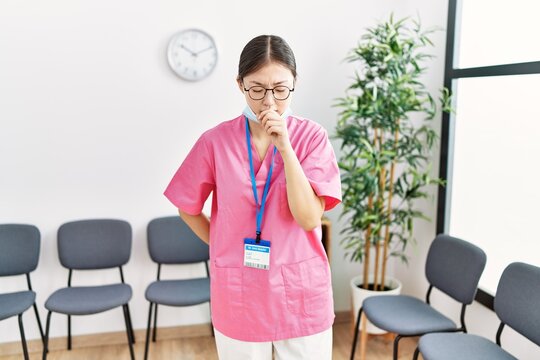 Young asian nurse woman at medical waiting room feeling unwell and coughing as symptom for cold or bronchitis. health care concept.