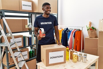 Young african american volunteer man packing donations box for charity looking away to side with smile on face, natural expression. laughing confident.