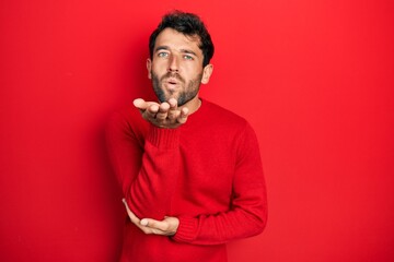 Handsome man with beard wearing casual red sweater looking at the camera blowing a kiss with hand...
