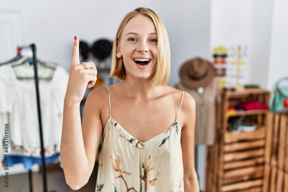 Sticker Young caucasian woman at retail shop pointing finger up with successful idea. exited and happy. number one.