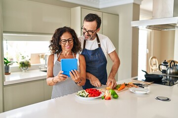 Middle age hispanic couple smiling confident cooking and using touchpad at kitchen