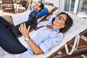 Middle age hispanic couple smiling confident lying on hammock with dog at terrace