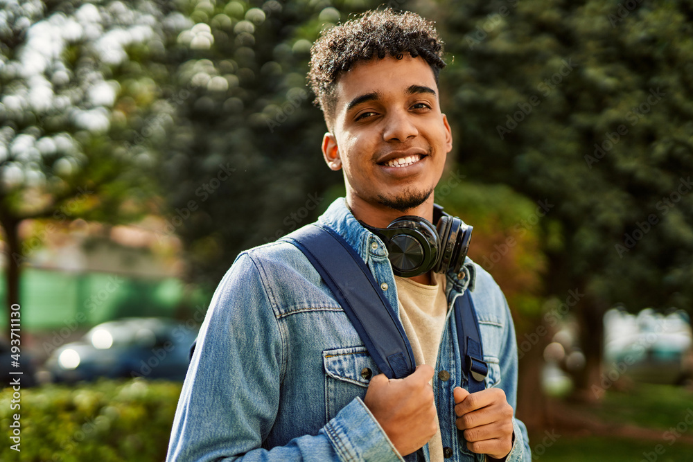 Wall mural Hispanic young man smiling wearing headphones at the university campus