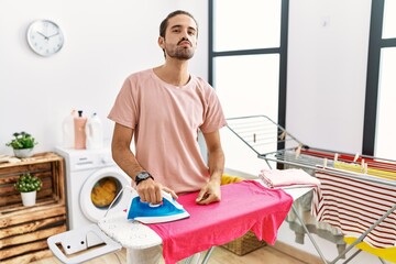 Obraz premium Young hispanic man ironing clothes at home looking at the camera blowing a kiss on air being lovely and sexy. love expression.