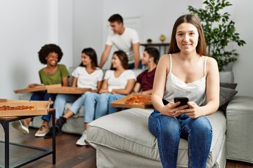 Group of young friends eating italian sitting on the sofa. Woman smiling and using smartphone at home.