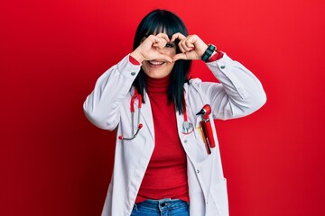 Young hispanic woman wearing doctor uniform and stethoscope doing heart shape with hand and fingers smiling looking through sign