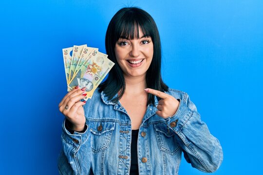 Young hispanic woman holding 50 romanian leu banknotes smiling happy pointing with hand and finger