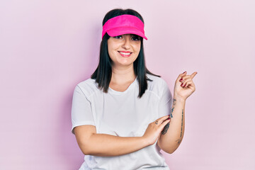 Obraz na płótnie Canvas Young hispanic woman wearing sportswear and sun visor cap smiling happy pointing with hand and finger to the side