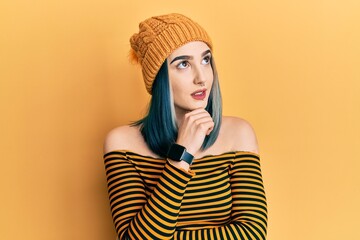 Young modern girl wearing wool hat with hand on chin thinking about question, pensive expression. smiling with thoughtful face. doubt concept.