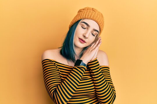 Young modern girl wearing wool hat sleeping tired dreaming and posing with hands together while smiling with closed eyes.