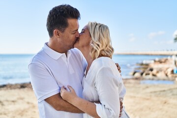 Middle age man and woman couple hugging each other and kissing standing at seaside